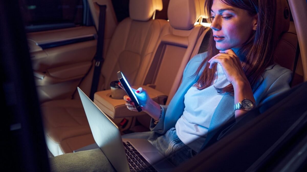 Woman using mobile phone and laptop in car