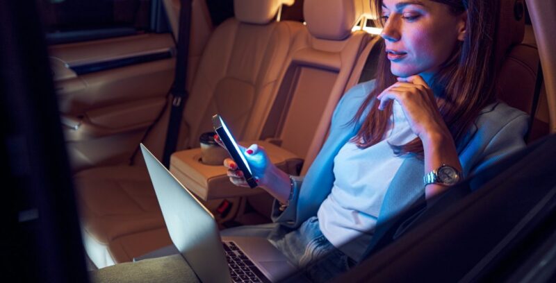 Woman using mobile phone and laptop in car