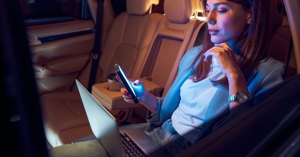 Woman using mobile phone and laptop in car