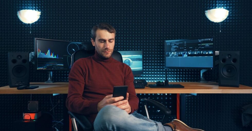 Young man working in the studio using a smartphone and computer. Young man working in the studio using a smartphone and computer.